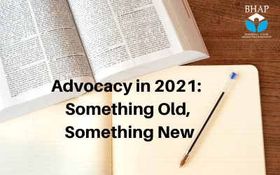 a desk with a legal book open and a notebook underneath it, with a pen on the notebook. Text reads, 'Advocacy in 2021: Something Old, Something New'